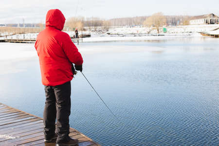 Winter, spring fishing on paid snow covered ice pond, lake in country club. Catching fish with spinner,bait, net.Fisherman with spinning rods.Men's hobby,entertainment,competition.Cold frozen weather.の写真素材
