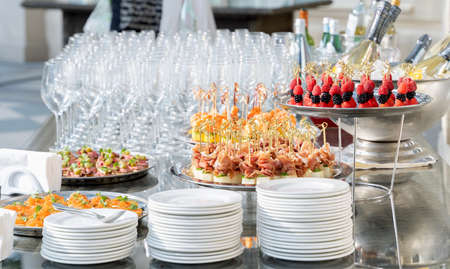 Wedding day recepton. Buffet table. Catering service. Plates with sweet canape with berries, raspberry, blackberry, ham,shrimp.Delicious gourmet food for guests.Many glasses,bottles of champagne,wine.の写真素材