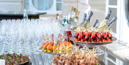 Wedding day recepton. Buffet table. Catering service. Plates with sweet canape with berries, raspberry, blackberry, ham,shrimp.Delicious gourmet food for guests.Many glasses,bottles of champagne,wine.の写真素材
