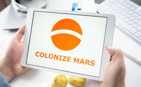 Russia Moscow 05.05.2021. Man holding tablet with logo of gaming platform Colonize Mars.Crypto coins, tokens mining online game.NFT staking system.Cryptocurrency stock exchange.Play, earn digital money.のeditorial素材