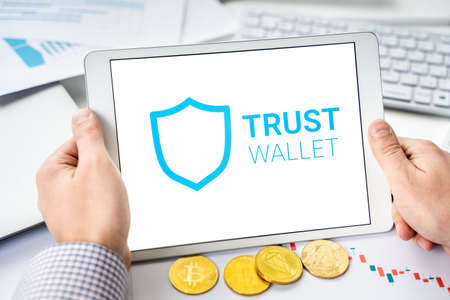 Russia Moscow 06.05.2021 Businessman, tablet. Logo of software cryptocurrency wallet, gateway Trust Wallet. Blockchain application to buy, store, send, swap crypto coins, digital tokens. Bitcoin, Ethereum.のeditorial素材