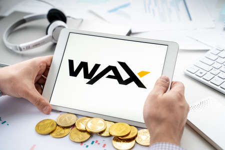 Russia Moscow 06.05.2021.Man holding tablet with logo of token, cryptocurrency WAX. Crypto coin for...