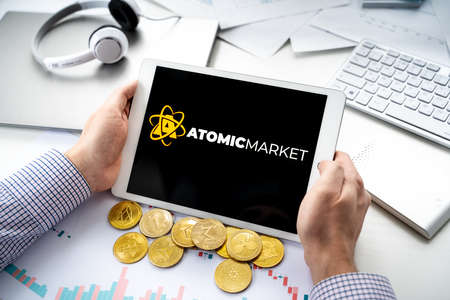 Russia Moscow 06.05.2021.Man holding tablet with logo of NFT marketplace Atomic market. Non fungible tokens for cryptocurrency WAX. Crypto coin for mining.Online game, gaming platforms.のeditorial素材