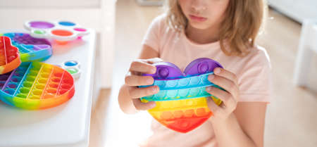 Little girl,kid,child plays with colorful children's room, bedroom.Funny trendy silicone antistress colorful sensory push toy.Flapping fidget.Rainbow color.Cure of autism.Stress reliever.の写真素材