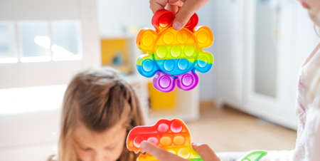 Little girls,kids,sisters play with colorful  children room,bedroom.Funny trendy silicone antistress colorful sensory push toy .Flapping fidget.Rainbow color.Cure of autism.Stress reliever.の写真素材