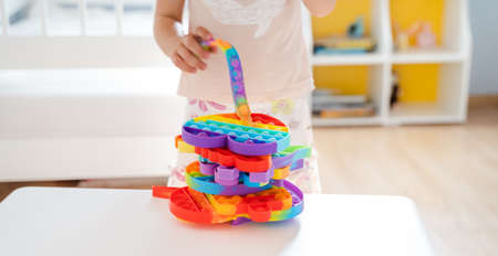 Little girl,kid,child plays with colorful  children's room, bedroom.Funny trendy silicone antistress colorful sensory push toyãFlapping fidget.Rainbow color.Cure of autism.Stress reliever.の写真素材