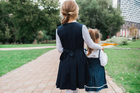 Back to elementary school concept. Little girl in school uniform goes to first grade with little sister on first of September. Ceremony of graduating. Last learning day, end of year.の写真素材