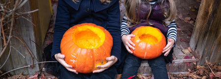 Little girls make jack-o-lantern from big pumpkins for celebratiion of halloween holiday.Witch costume, hat, coat. Cut with knife,take out pulp with seeds.Outdoors activity, backyard.Children's party.の写真素材