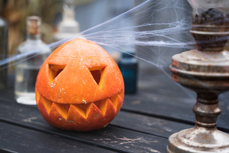 Orange pumpkin for halloween, jack-o-lantern with scary carved eyes, mouth.Candles, old lamp, spiderweb on wooden table near barn. DIY home,street decoration, entertainment for children, horror.の写真素材