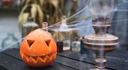 Orange pumpkin for halloween, jack-o-lantern with scary carved eyes, mouth.Candles, old lamp, spiderweb on wooden table near barn. DIY home,street decoration, entertainment for children, horror.の写真素材