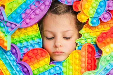 Little girl,kid,child plays with colorful children's room, bedroom.Funny trendy silicone anti stress colorful sensory push toy .Flapping fidget.Rainbow color.Cure of autism.Stress reliever.の写真素材