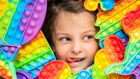Little girl,kid,child plays with colorful children's room, bedroom.Funny trendy silicone anti stress colorful sensory push toy .Flapping fidget.Rainbow color.Cure of autism.Stress reliever.の写真素材