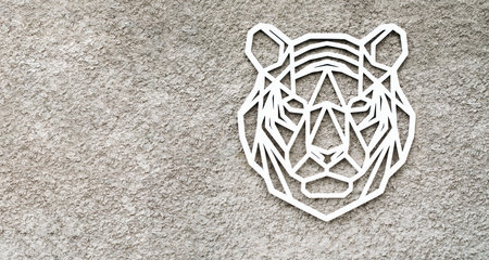 Large flat white tiger head on gray rough stone wall, plaster background. Wooden beautiful figure, winter symbol of New Year and Christmas holiday 2022. Creative design for celebration in interior.の写真素材