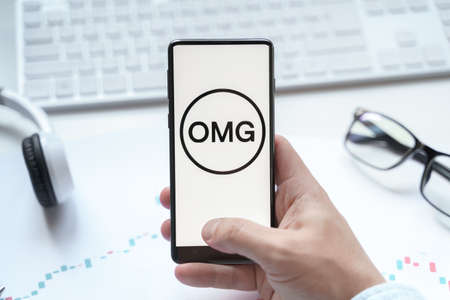 Russia Moscow 08.06.2021. Logo with OMG, OmiseGO Network in mobile phone. Value transfer network for ETH and ERC20 tokens.のeditorial素材