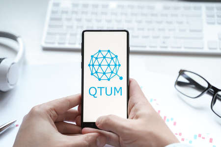 Russia Moscow 08.06.2021 Logo of cryptocurrency QTUM, quantum crypto coin in mobile phone. Blockchain technology designed to merge the smart contract element of Ethereum.のeditorial素材