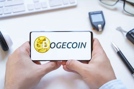 Russia Moscow 12.06.2021 Logo of Dogecoin coin in mobile phone. Cryptocurrency XMR token. Trading blockchain platform to buy,sell on decentralized exchange DEX. Digital money.Business,investing.のeditorial素材