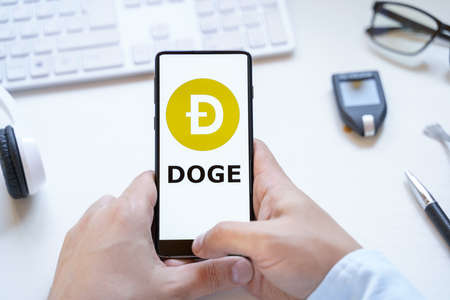 Russia Moscow 12.06.2021 Logo of Dogecoin coin in mobile phone. Cryptocurrency XMR token. Trading blockchain platform to buy,sell on decentralized exchange DEX. Digital money.Business,investing.のeditorial素材