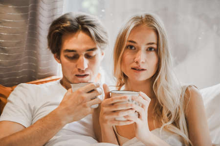 Young just married couple traveling in camper,house on wheels,trailer,motor home.Love romantic road travel,freedom life. Small bed,bedroom in van.Wanderlust vacation,weekend. Girl,guy,happy adventure. Drinking tea, coffee, hot chocolate from cup, mugの写真素材