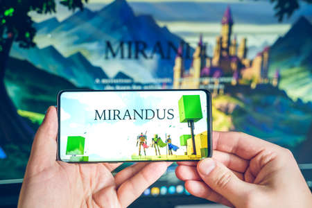 Russia Moscow 25.12.2021 Logo of Mirandus. Blockchain nft ethereum cryptocurrency strategy game. Man playing in laptop,mobile phone. Crypto coin, token. Earning digital money.Play-to-earn.のeditorial素材