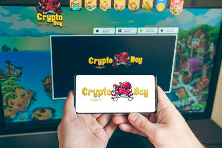 Russia Moscow 25.12.2021 Logo of Cryptobay. PVP,PVE token, blockchain nft ethereum cryptocurrency strategy game in laptop,mobile phone.Man playing for crypto coin. Earning digital money. Play-to-earn.のeditorial素材