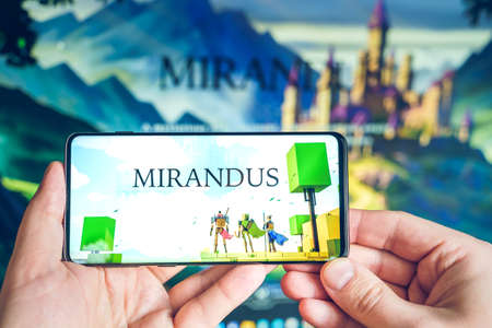 Russia Moscow 25.12.2021 Logo of Mirandus. Blockchain nft ethereum cryptocurrency strategy game. Man playing in laptop,mobile phone. Crypto coin, token. Earning digital money.Play-to-earn.のeditorial素材