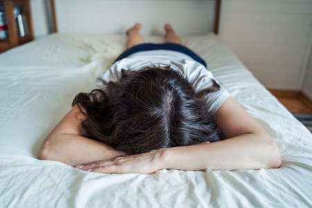 Sad, unhappy woman lying on bed in depression. Headache, stress, anxiety, tension, psychological...