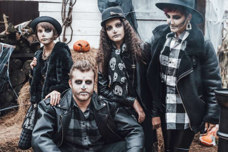 Scary family, mother, father, daughters celebrating halloween. Terrifying black skull half-face makeup and witch costumes, stylish images.Horror,fun at children's party in barn on street.Hats,jackets.の写真素材