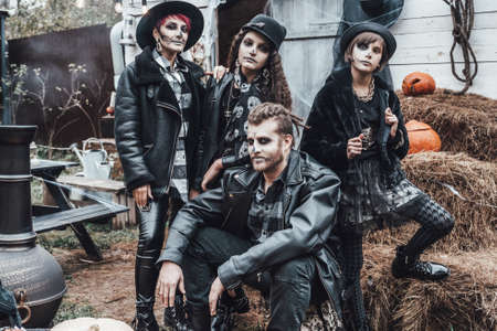 Scary family, mother, father, daughters celebrating halloween. Terrifying black skull half-face makeup and witch costumes, stylish images.Horror,fun at children's party in barn on street.Hats,jackets.の写真素材