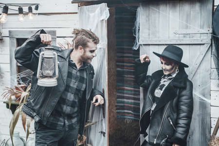 Scary love family couple man, woman celebrating halloween.Terrifying black skull half-face makeup,witch costumes,stylish images,jacket,hat.Horror,fun at photoshoot, holiday party near barn on street.の写真素材