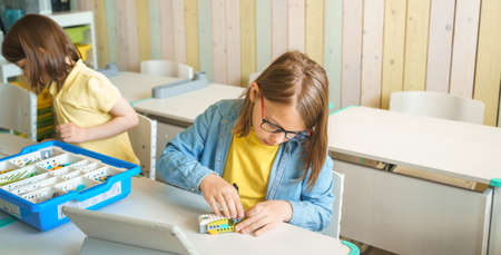 Programming work, learning robotics in elementary school. Children students assembly, launch, coding of robot. Constructor parts by instructions in tablet. STEM education science engineering class.の写真素材