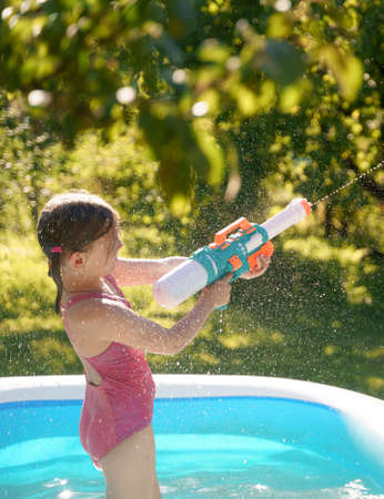Little girl in swimwear, daughter and dad, daddy, father swim and play water pistols, guns in...