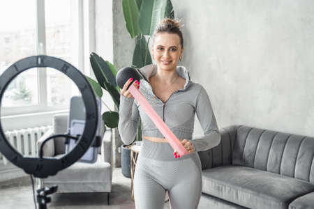 Sporty slim woman yoga coach, fitness instructor records video of online yoga training in mobile...