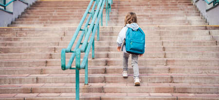 Back to elementary, primary school. Little girl with big backpack goes in hurry, late to first grade...