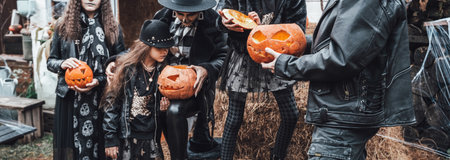 Scary family, mother, father, daughters celebrating halloween. Terrifying black skull half-face makeup and witch costumes, stylish images.Horror,fun at children's party in barn on street.Hats,jackets.の写真素材