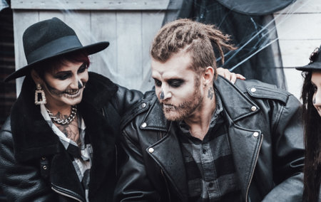 Scary family, mother, father, daughters celebrating halloween. Terrifying black skull half-face makeup and witch costumes, stylish images.Horror,fun at children's party in barn on street.Hats,jackets.の写真素材