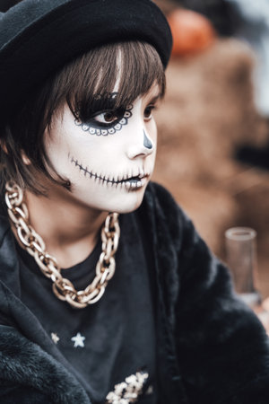 Beautiful scary little girl celebrating halloween. Terrifying black, white half-face makeup and...