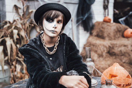 Beautiful scary little girl celebrating halloween. Terrifying black, white half-face makeup and...