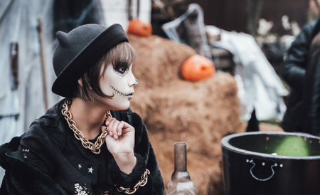 Beautiful scary little girl celebrating halloween. Terrifying black, white half-face makeup and...