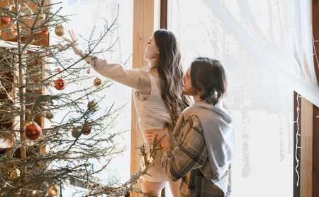 Hugging stylish love couple girl, guy lie on skin on floor in cozy wooden country house,chalet in winter forest.Celebrating new year eve.Gifts,family holiday.Romantic weekend.Decorated Christmas tree.の写真素材