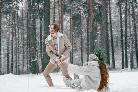 Sledging love romantic young couple girl,guy in snowy winter forest with christmas tree, sled.Walking with sleigh in stylish clothes,fur coat,jacket,woolen shawl.Snow lovestory.Romantic date,weekend.の写真素材