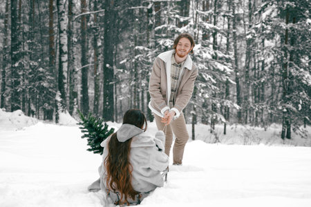 Sledging love romantic young couple girl,guy in snowy winter forest with christmas tree, sled.Walking with sleigh in stylish clothes,fur coat,jacket,woolen shawl.Snow lovestory.Romantic date,weekend.の写真素材