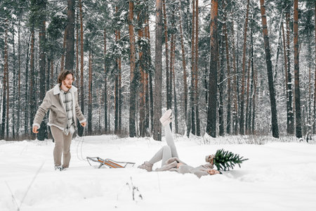 Sledging love romantic young couple girl,guy in snowy winter forest with christmas tree, sled.Walking with sleigh in stylish clothes,fur coat,jacket,woolen shawl.Snow lovestory.Romantic date,weekend.の写真素材
