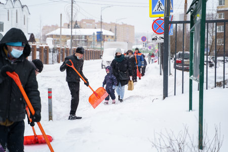 Russia Moscow 13.02.2021 Street cleaners, men clean snow from road, sidewalk with large shovels. City winter weather collapse, snowfall, snowdrifts. Car traffic jam. Heavy snowstorm, blizzard.のeditorial素材