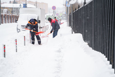 Russia Moscow 13.02.2021 Street cleaners, men clean snow from road, sidewalk with large shovels. City winter weather collapse, snowfall, snowdrifts. Car traffic jam. Heavy snowstorm, blizzard.のeditorial素材