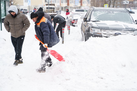 Russia Moscow 13.02.2021 Street cleaners, men clean snow from road, sidewalk with large shovels. City winter weather collapse, snowfall, snowdrifts. Car traffic jam. Heavy snowstorm, blizzard.のeditorial素材