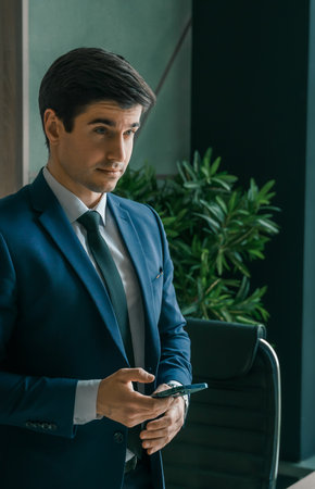 Businessman in suit with mobile phone in hands. Man typing message, using social net. Checking news. Making business meeting. Modern office.General manager,ceo.Calling to partner.Planning working day.の写真素材