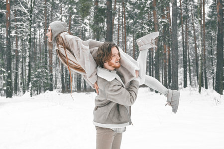 Love romantic young couple. Guy spinning girl in snowy winter forest with trees. Walking, having fun, laughing in stylish clothes, fur coat, jacket, woolen shawl. snow love story. Romantic date,weekend.の写真素材