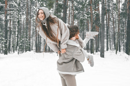 Love romantic young couple. Guy spinning girl in snowy winter forest with trees. Walking, having fun, laughing in stylish clothes, fur coat, jacket, woolen shawl. snow love story. Romantic date,weekend.の写真素材