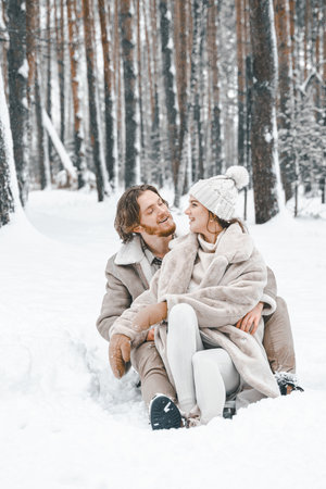 Love romantic young couple girl,guy in snowy winter forest sledding,playing.Walking with sleigh in stylish clothes, fur coat,jacket, woolen shawl,bonnet.Snow love story.Romantic date,weekend.の写真素材