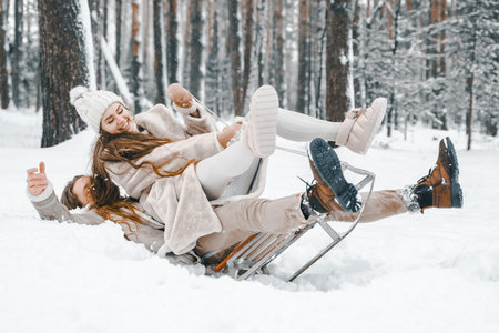 Love romantic young couple girl,guy in snowy winter forest with christmas tree, sled.Walking with sleigh in stylish clothes, fur coat,jacket, woolen shawl, bonnet.Snow love story.Romantic date,weekend.の写真素材